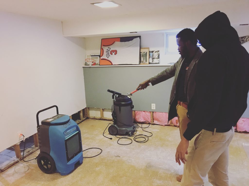 expert from water damage company pointing out water damage to client with industrial machines on the floor