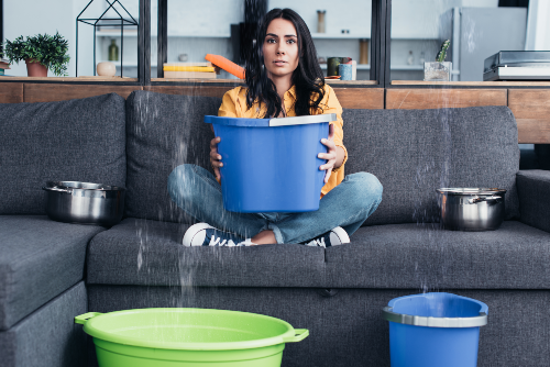 woman sitting on couch holding bucket under leak