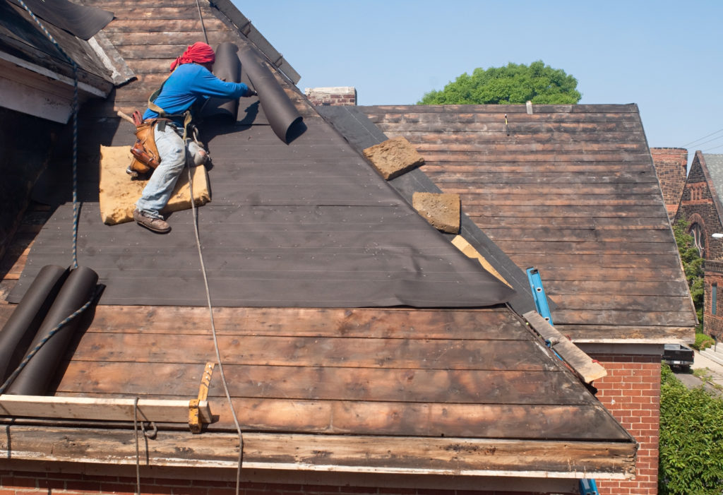 roofer laying underlayer on roof during roof damage repair