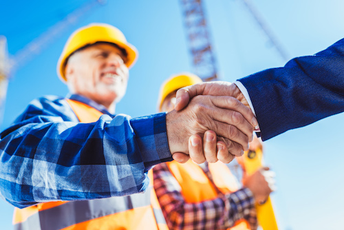 Handshake between builder wearing yellow hardhat and businessman with crane in the background
