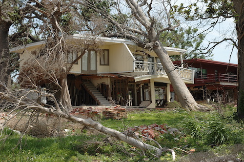 fallen tree laying on two-story house with debris in the yard before a storm damage inspection
