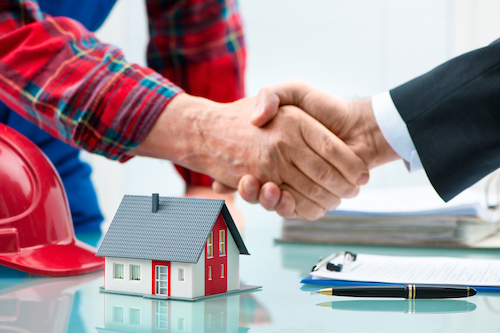 Handshakes with customer after contract signature with hardhat and miniature house on table