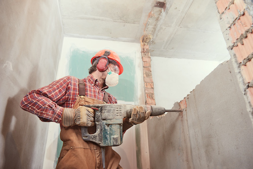Worker with personal protection equipment and demolition hammer at service for interior brick wall construction breaking in building industry