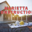 Marietta construction written in red over exterior view of home with table supporting hardhats and blueprints with the sun rising in the background