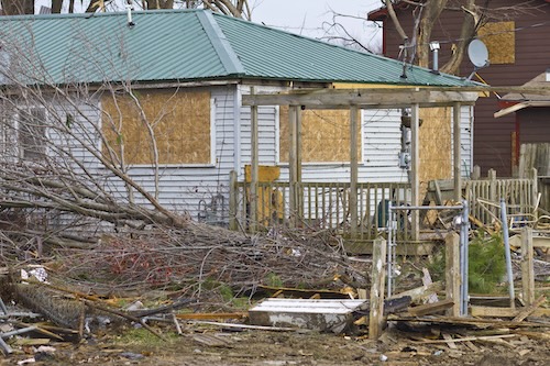 wind blown trees in front of house with boarded windows